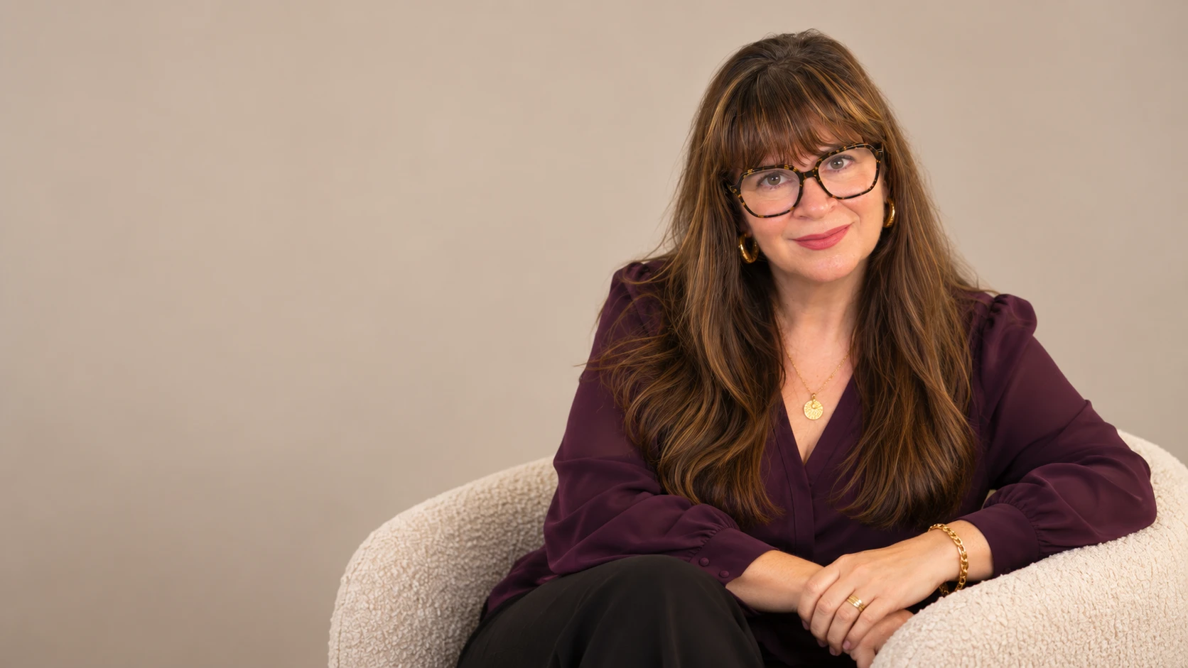 Dr. Alison Feit in a plum blouse seated in a chair against a warm beige backdrop
